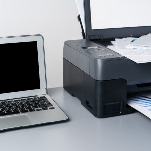 Printer and laptop on grey table in office close up